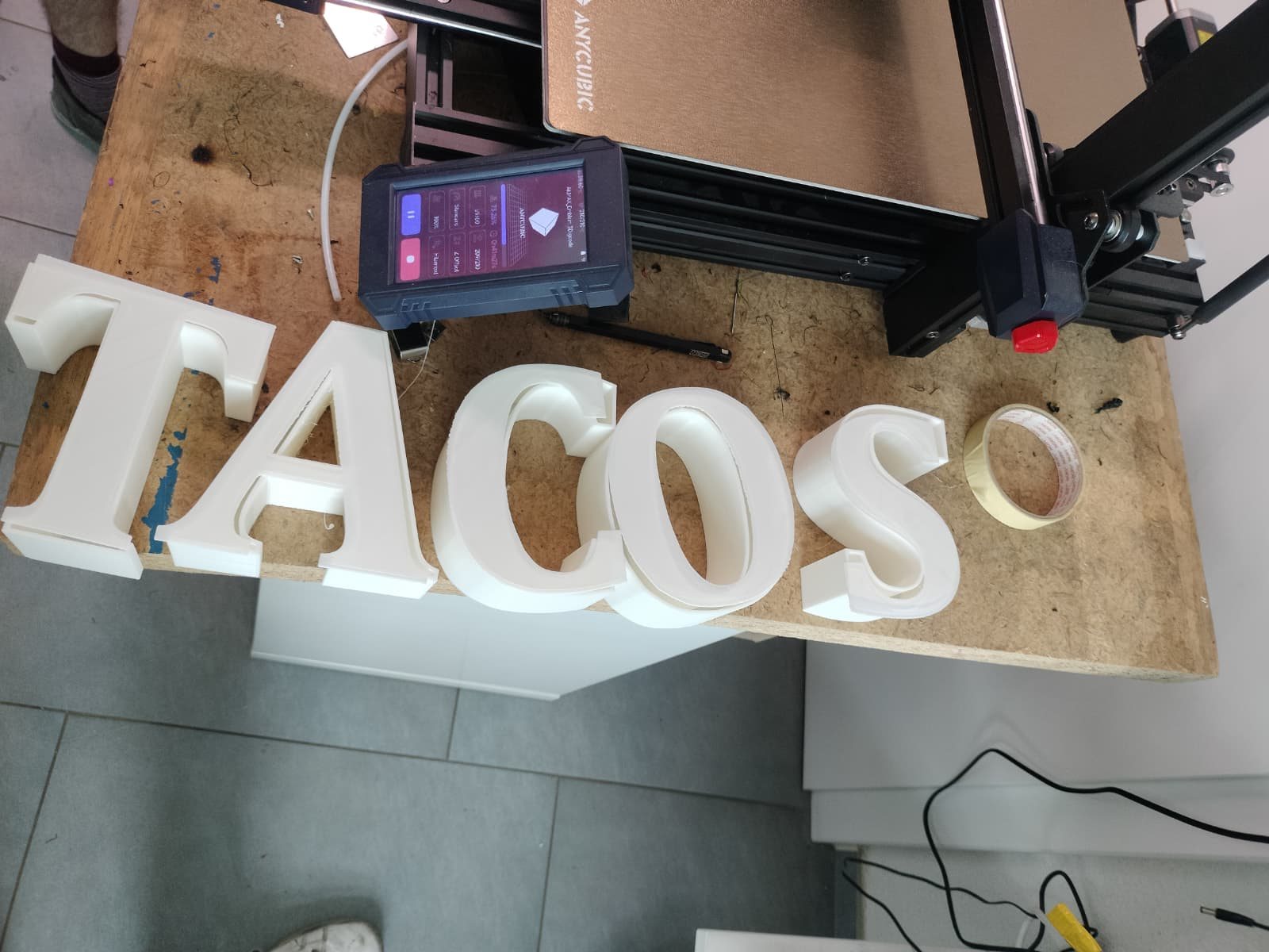 Gedruckte Buchstaben «TACOS» auf der Werkbank neben dem 3D-Drucker