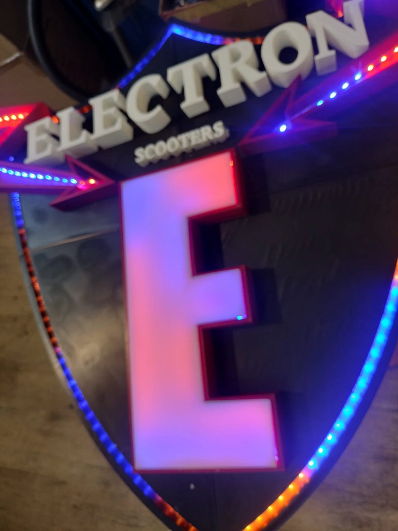 Nahaufnahme des Schilds «Electron Scooters» mit leuchtendem E und LED-Rand